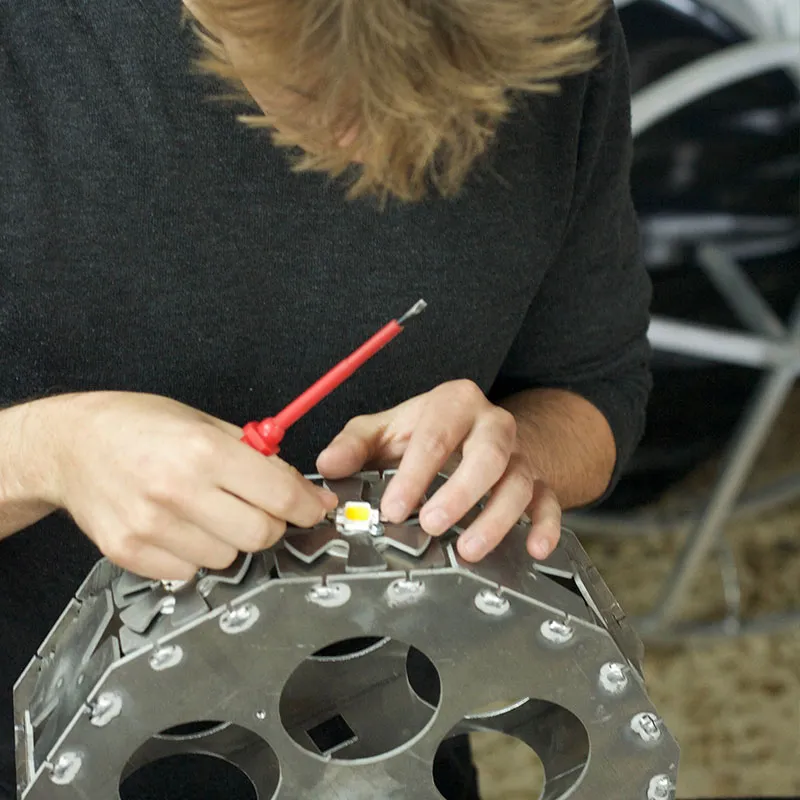 Manos atornillando un módulo LED sobre el disipador circular de aluminio de una lámpara